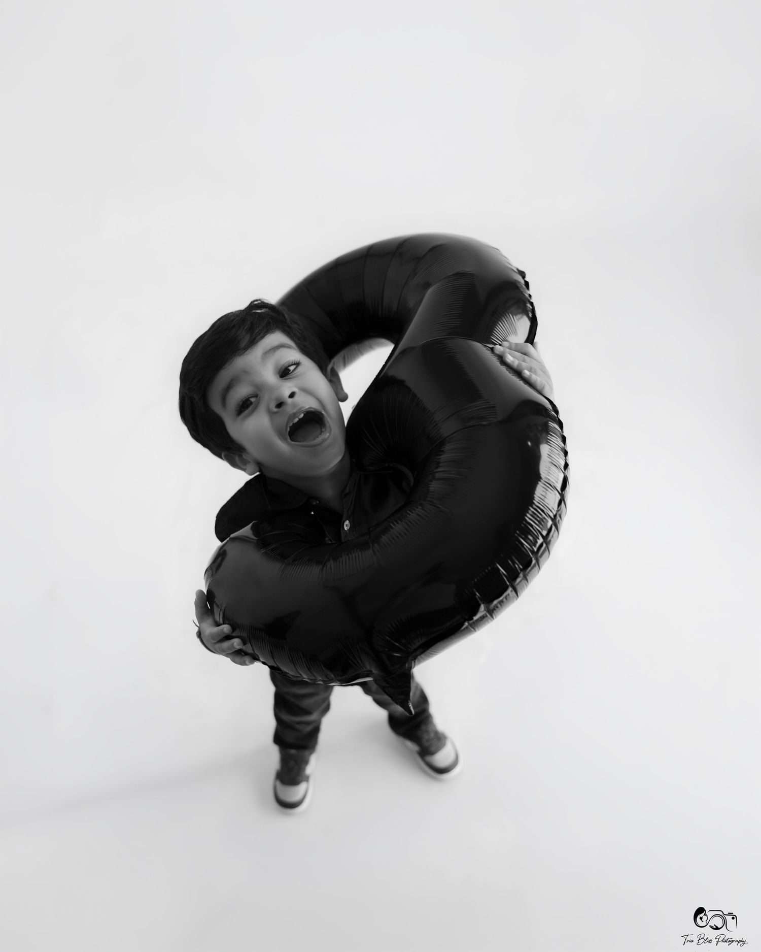 Black and white photo of a joyful child holding a large inflatable ring above their head, wearing a cap and sneakers.