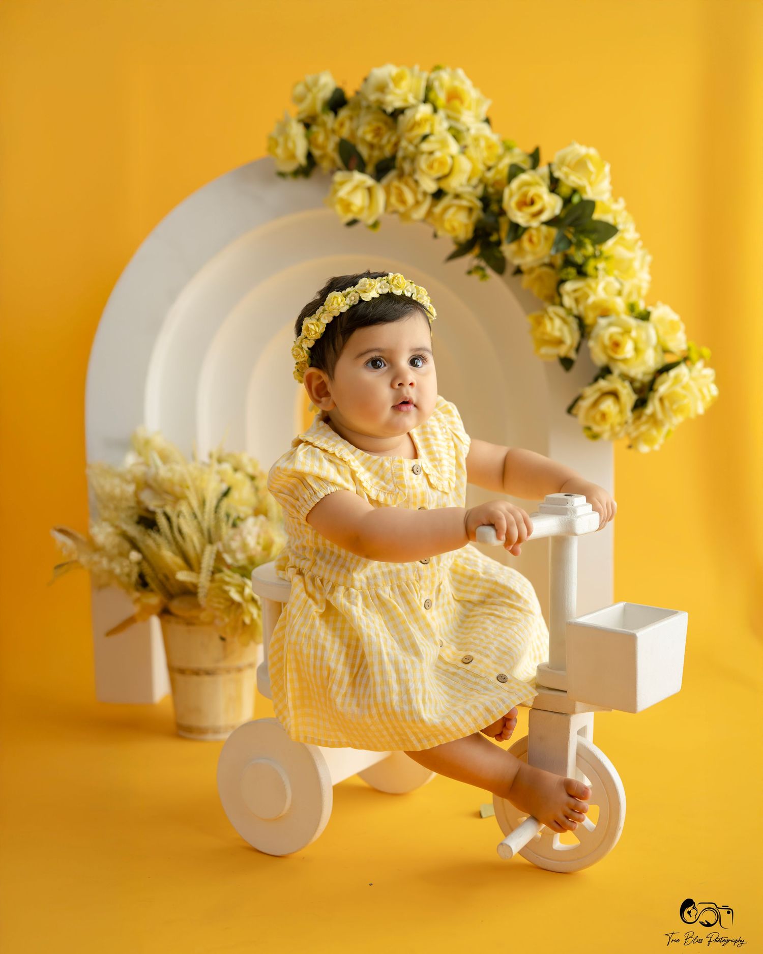 Baby in yellow dress lying on white surface with yellow roses in background in springtime portrait series.
