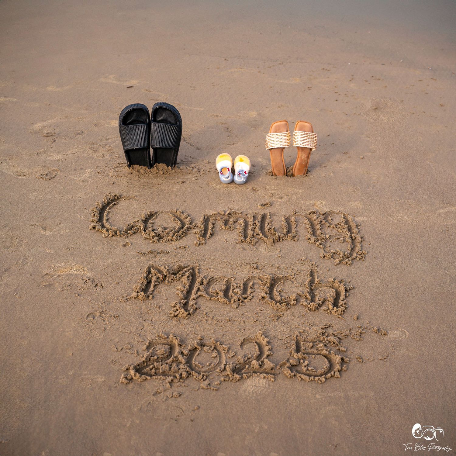 Beach sand pregnancy announcement reading Coming March 2025 with adult sandals and tiny baby shoes above the text.