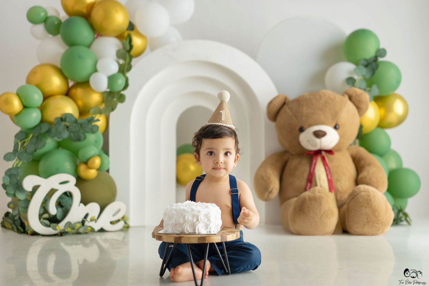Green and gold balloon decorations with a teddy bear accent for a first birthday party celebration setup.