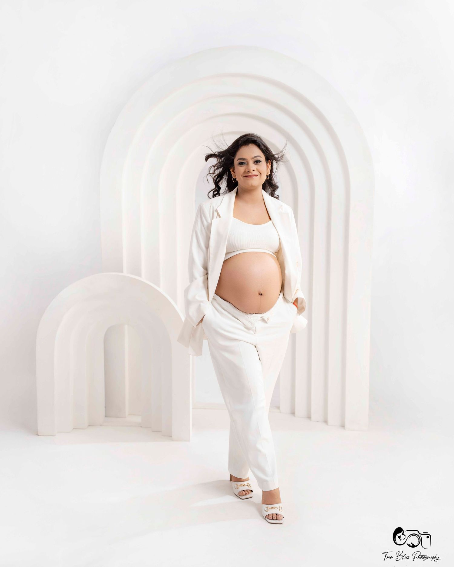 A maternity photo series in a white arched hallway setting shows a woman in flowing white clothing striking dynamic poses.