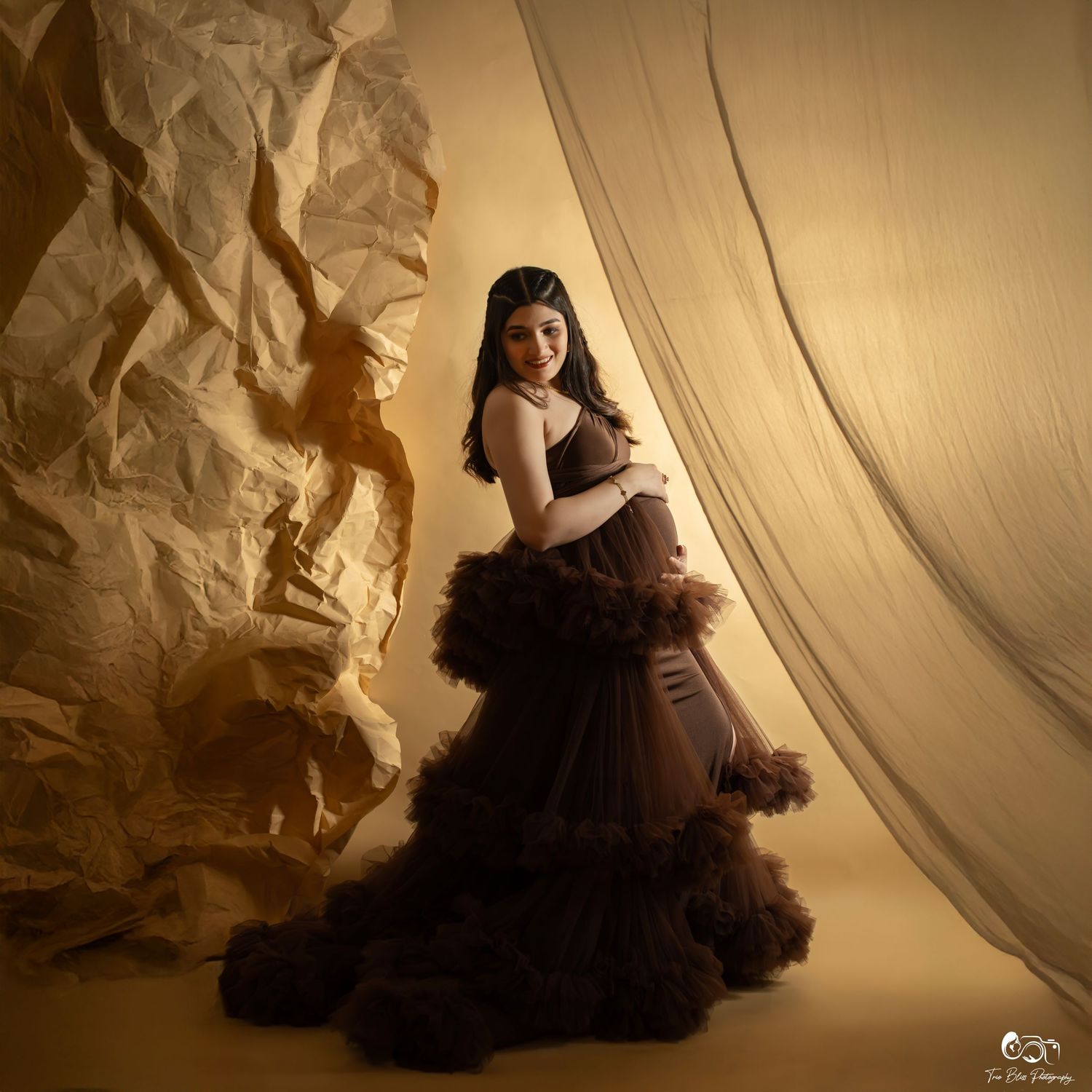 A flowing tulle dress in black creates dramatic silhouettes against a warm sepia-toned studio backdrop.