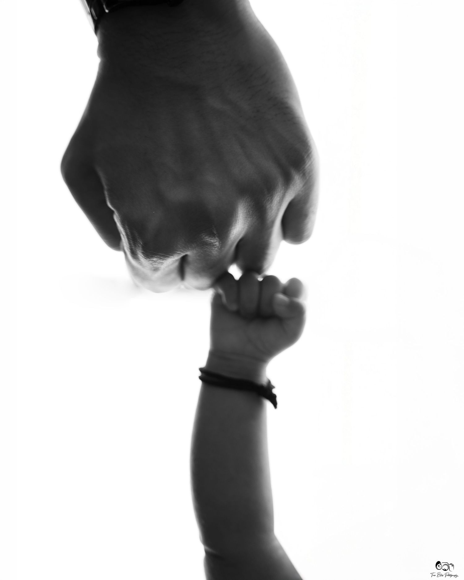 Black and white photo of an adult hand gently holding a newborn baby's tiny fist, symbolizing love and connection.