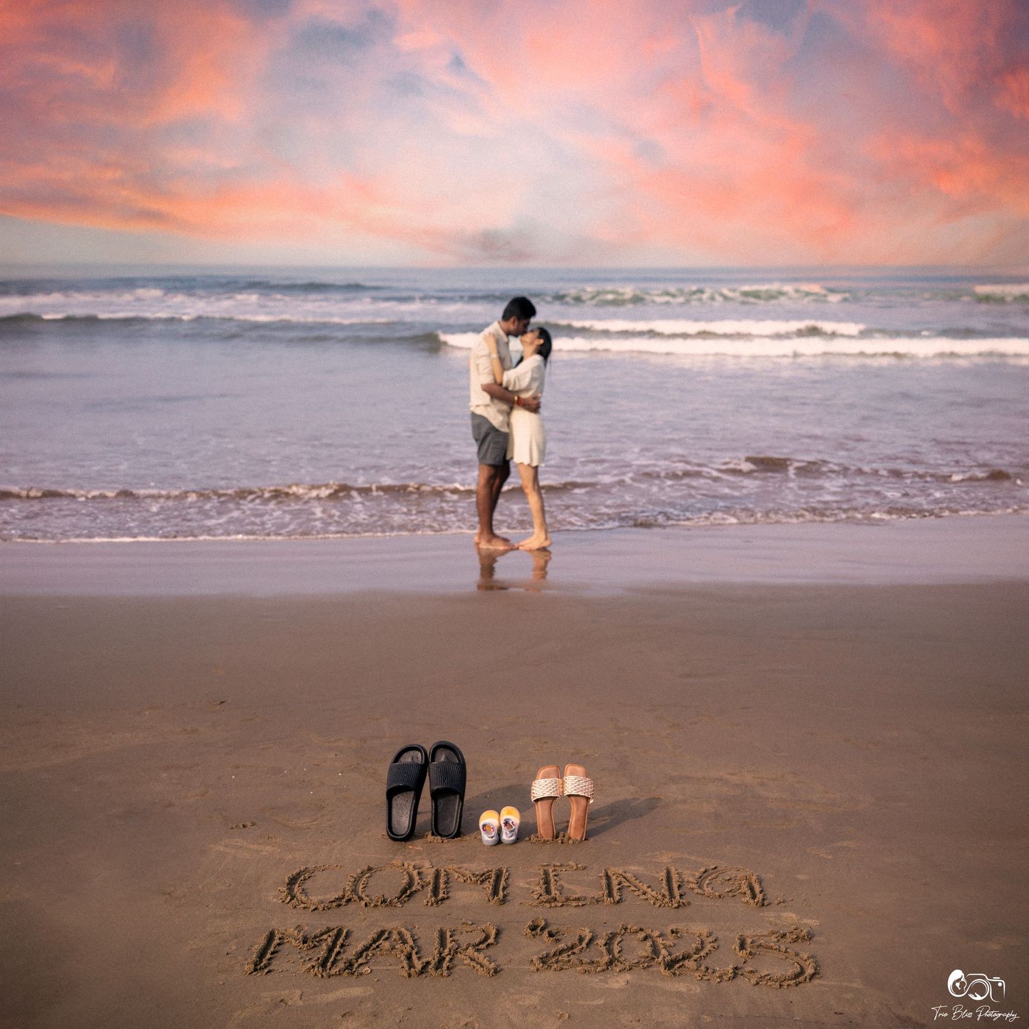 Couple kissing on a beach at sunset with sandals and names written in sand, romantic engagement photo.