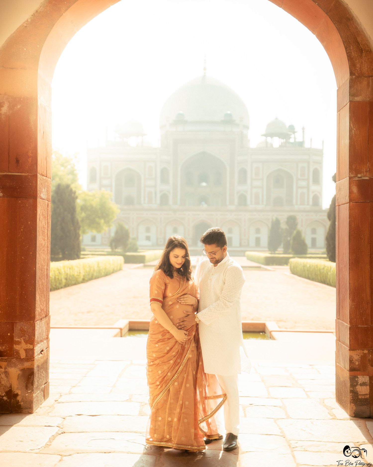 Couple in traditional Indian attire poses under arch at Humayun's Tomb, Delhi, during a maternity photoshoot.