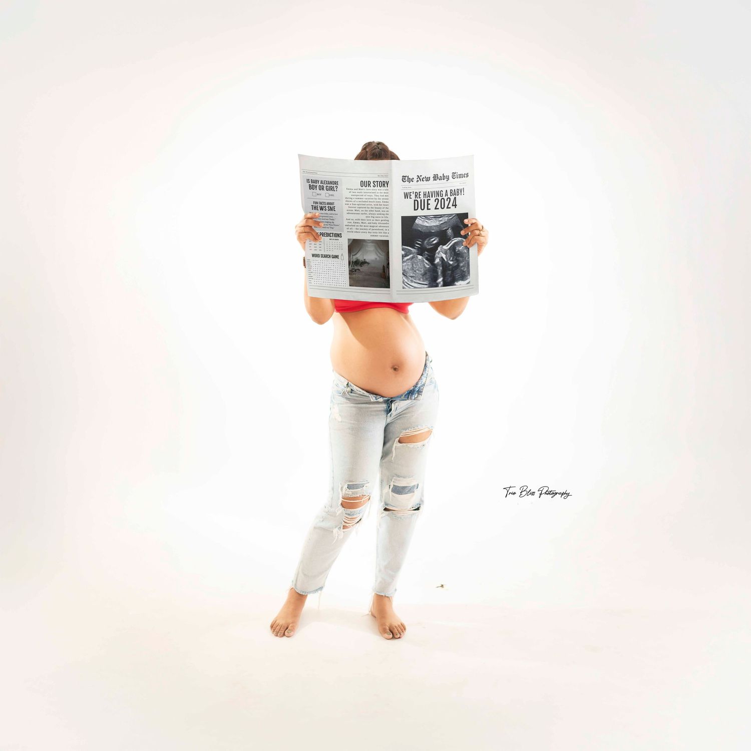 Person in distressed jeans and white shirt sits on floor reading a newspaper against white background.
