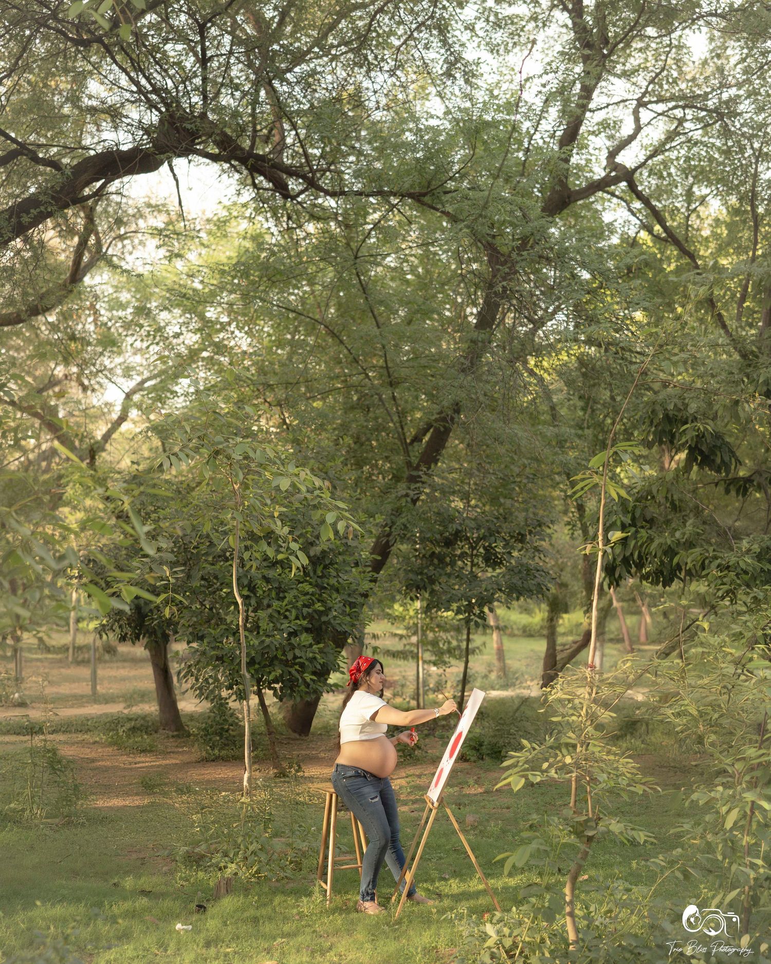 Artist painting on canvas outdoors in a lush green park surrounded by tall trees on a serene day.