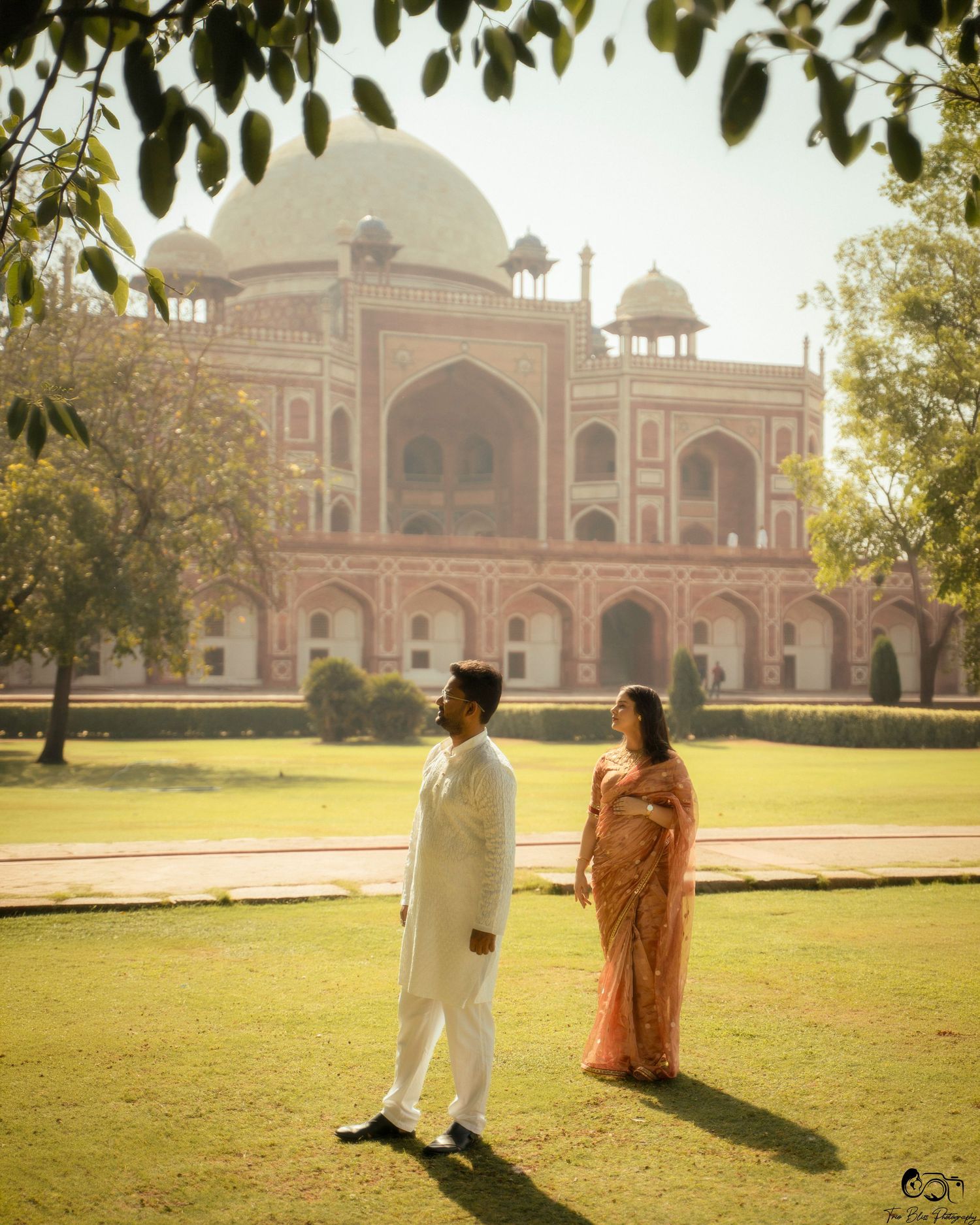 Couple in traditional Indian attire posing at Humayun's Tomb, Delhi, with lush green gardens in the background.