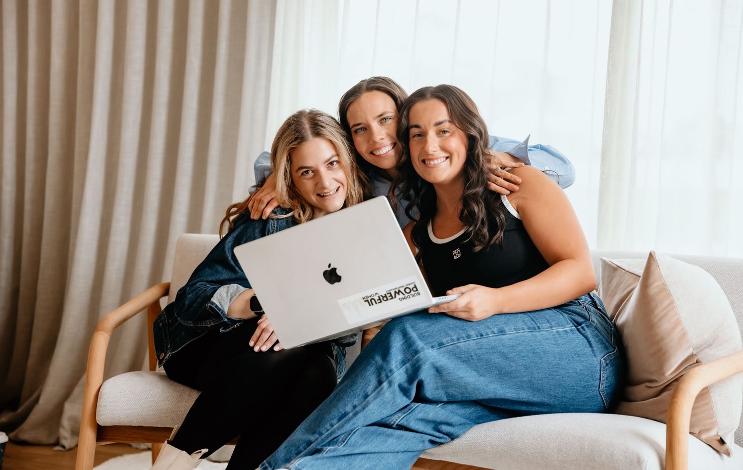 Three friends sharing laptop while relaxing on cozy beige couch.