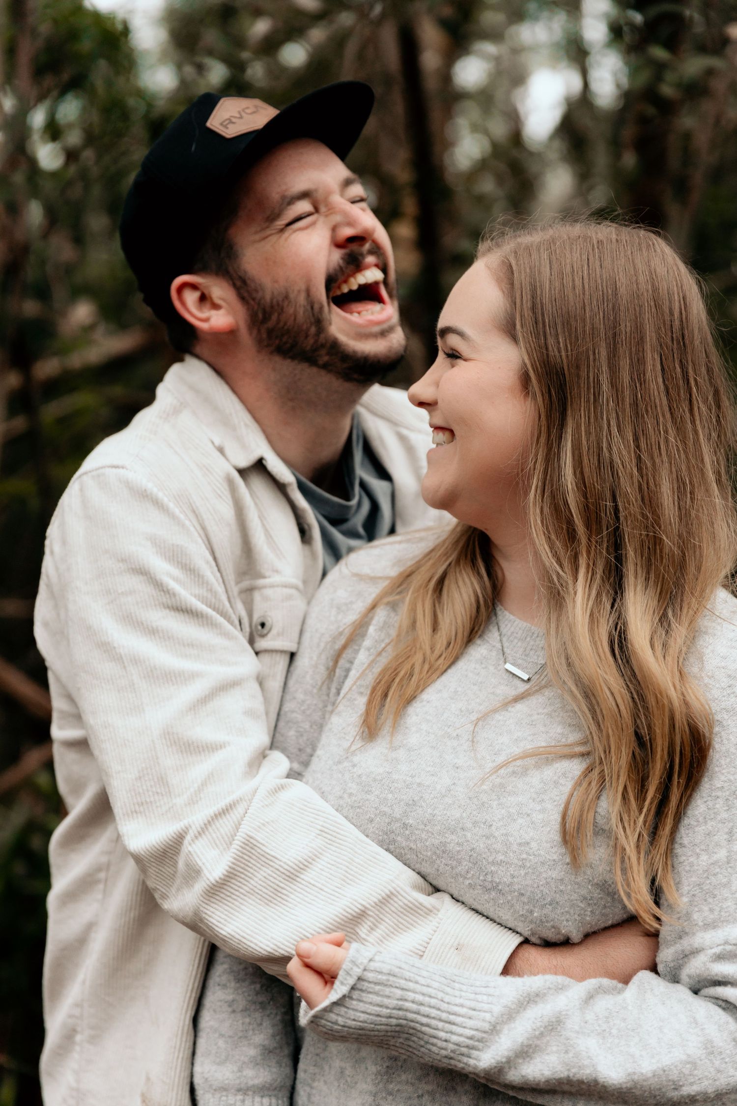A candid moment of shared laughter between two people in casual attire against a natural backdrop.