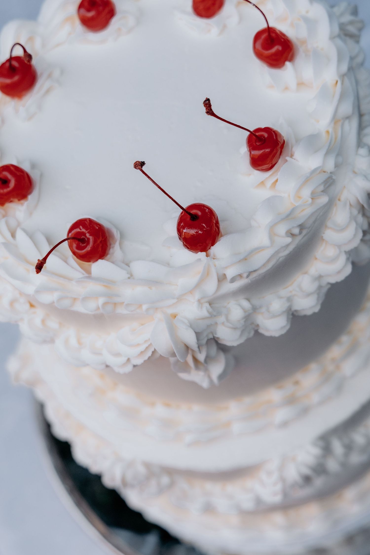 Elegant white tiered wedding cake decorated with swirled frosting and bright red maraschino cherries on top.