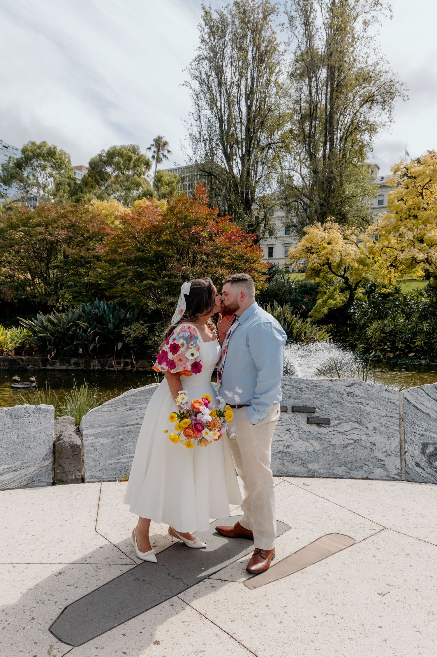 A couple shares a romantic moment together on a stone terrace surrounded by autumn foliage in the background.
