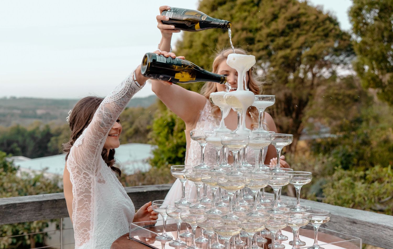 Champagne tower being carefully arranged with glassware at an elegant outdoor wedding reception.