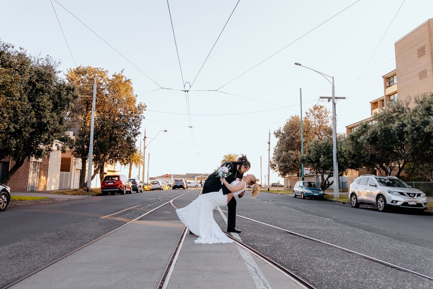 Bride and groom share a romantic dip kiss on a tram track street in Melbourne on their wedding day.