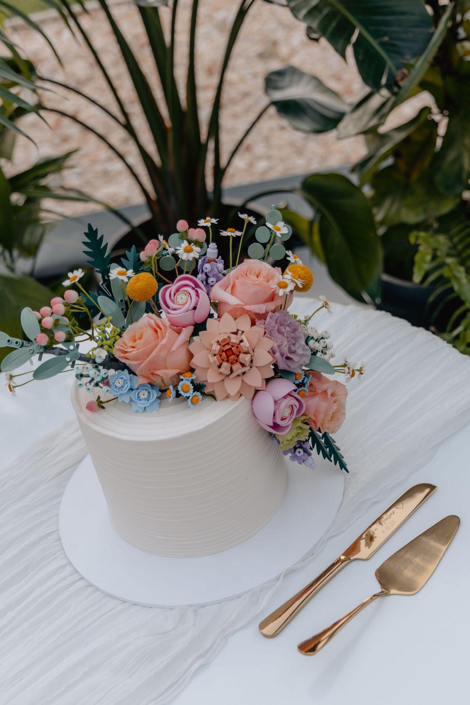 Elegant floral centerpiece with pink roses and mixed flowers in white ceramic bowl with gold cutlery on white tablecloth.