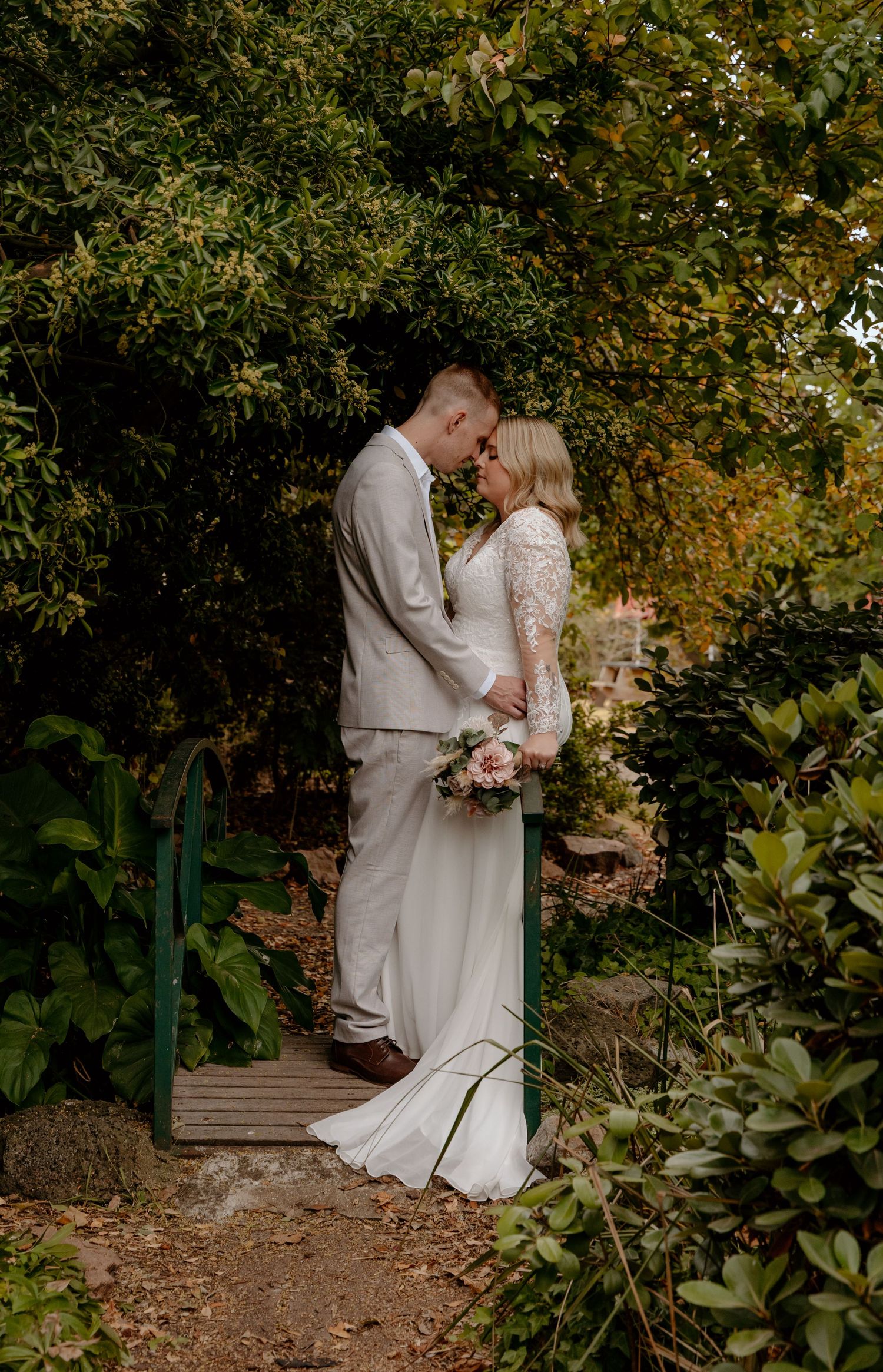 Bride and groom share a tender moment on a garden bridge surrounded by lush greenery on their wedding day.