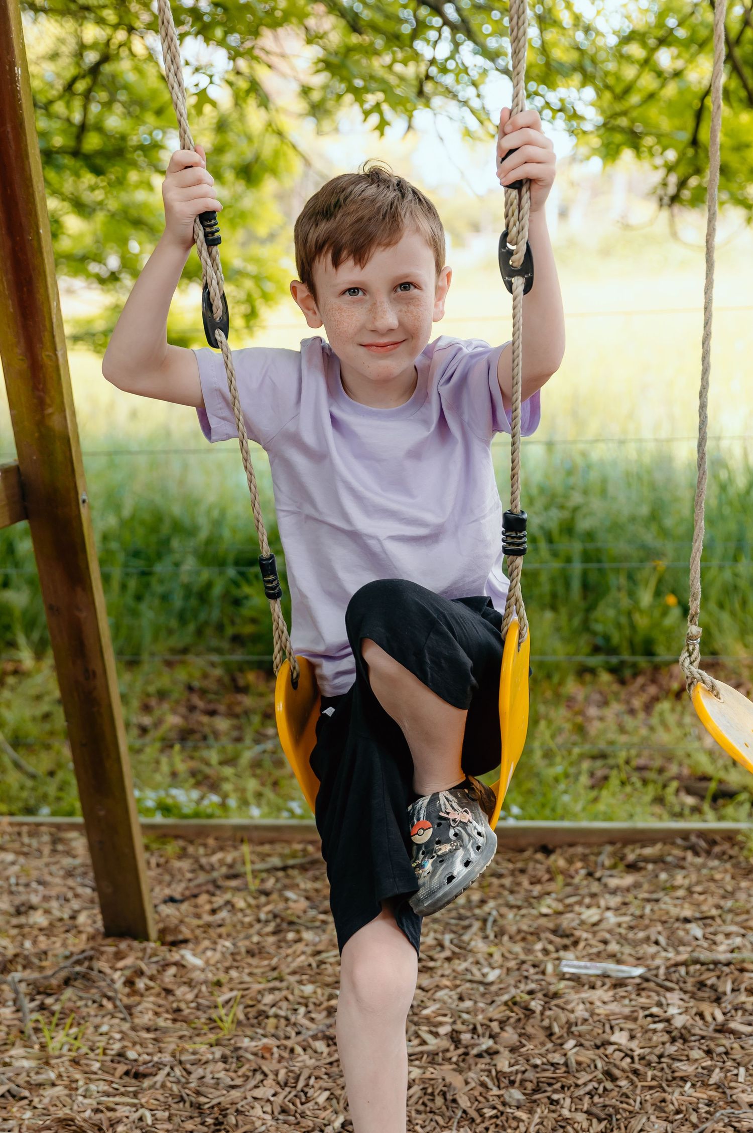 Child enjoying playtime on a yellow swing set in a sunny backyard.