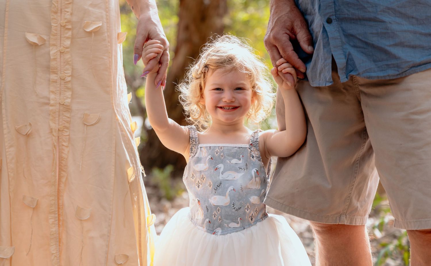 Child in sparkly dress holds hands up while dancing outdoors.
