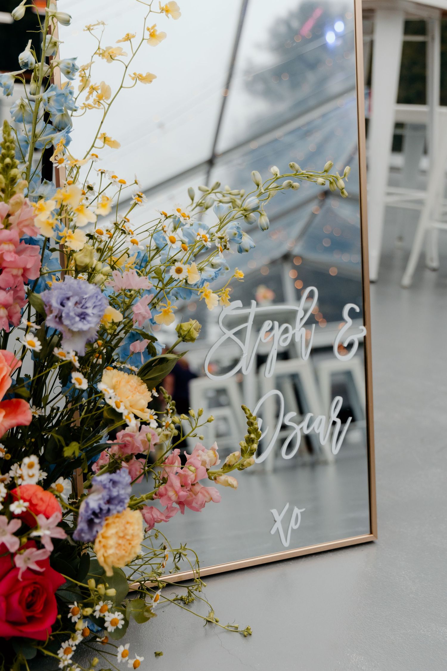 A floral arrangement with colorful blooms frames a mirror with elegant script writing on its surface.