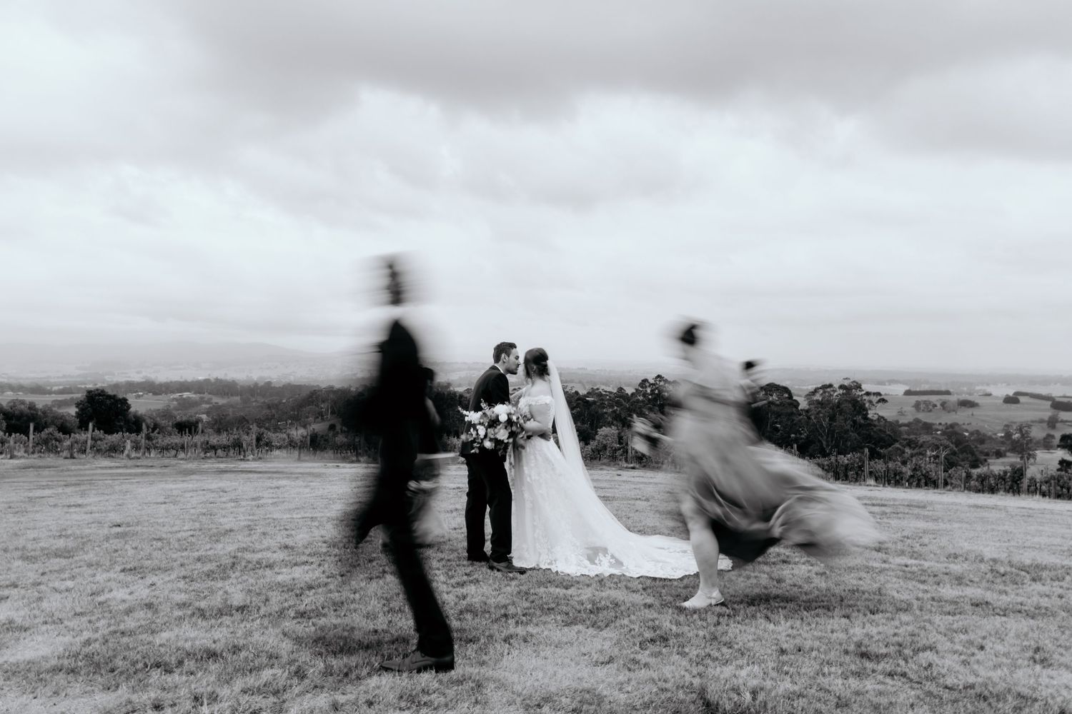 Artistic black and white motion blur photo of wedding ceremony participants in a scenic outdoor field.