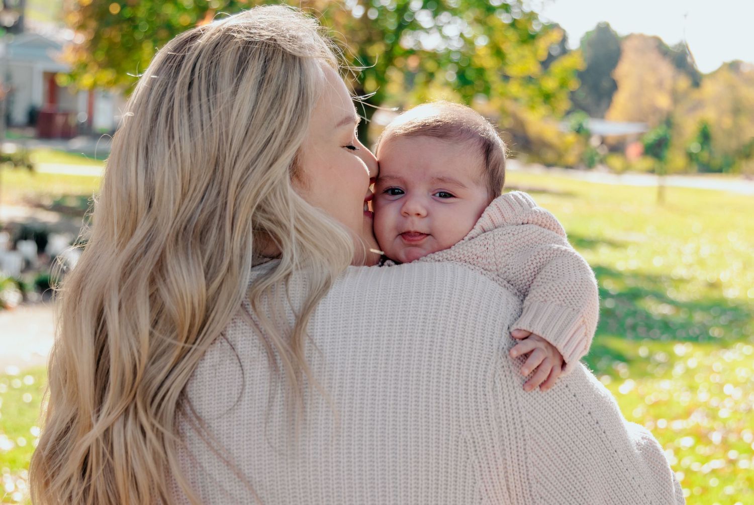 A tender moment shared between parent and baby outdoors on an autumn day with fallen leaves in the background.