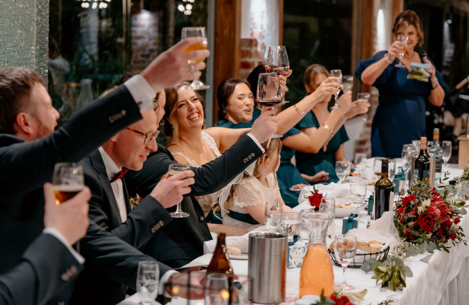 Wedding guests raise their glasses in a toast during an elegant reception celebration at a rustic brick venue.