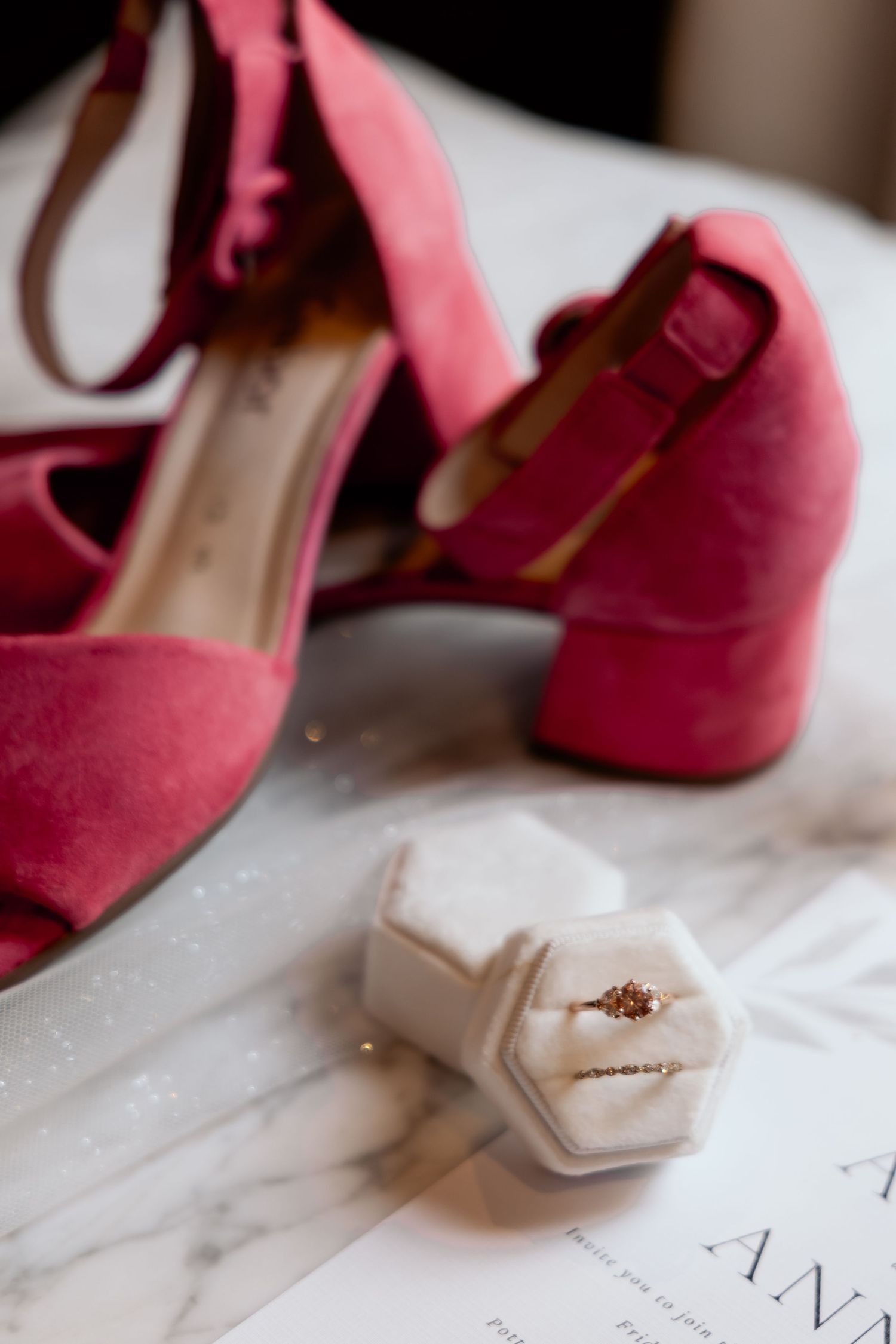 Pink and burgundy suede shoes arranged on white marble surface for product photography.