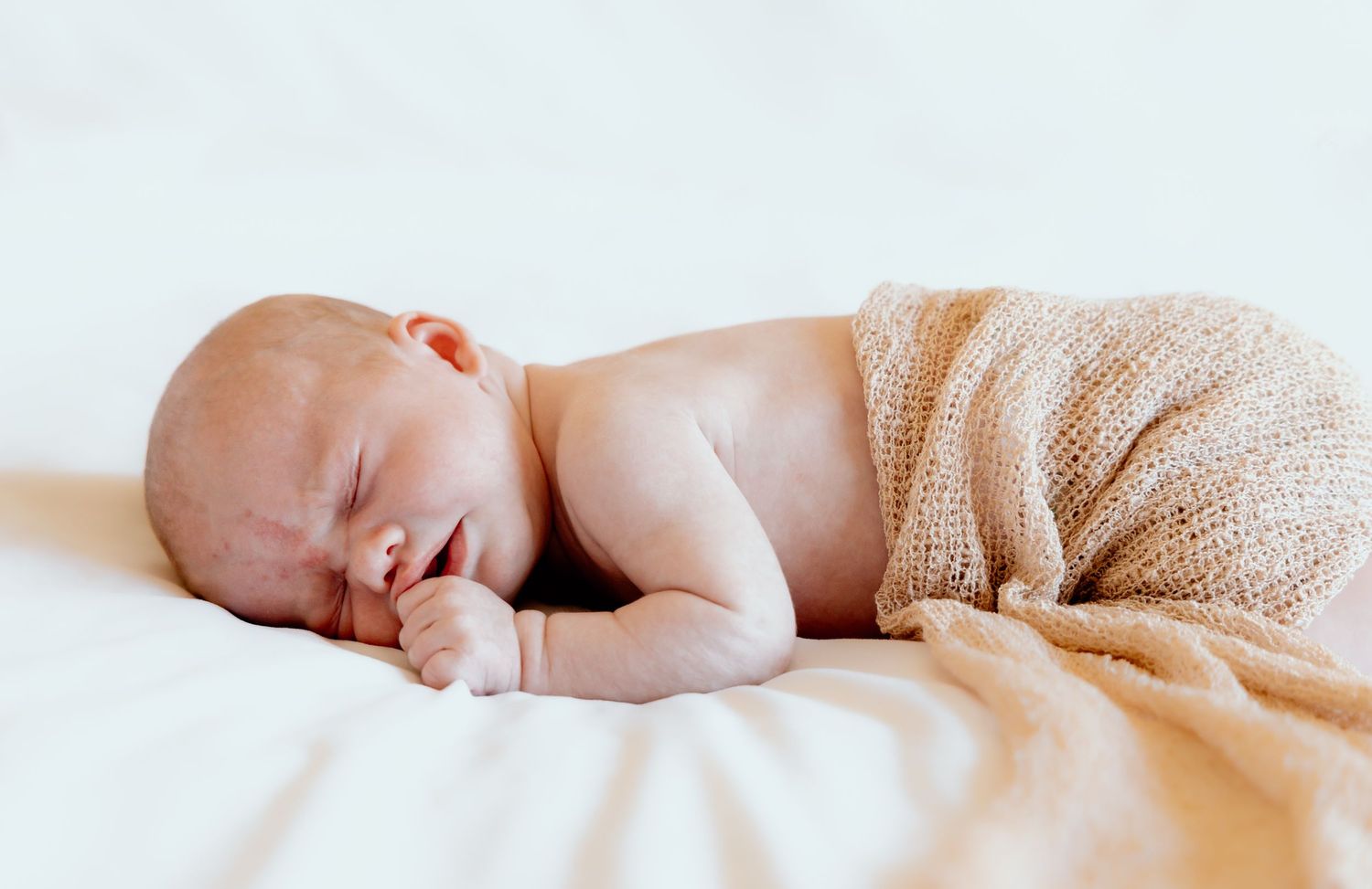 Peaceful newborn baby sleeping under beige blanket on white bedding.