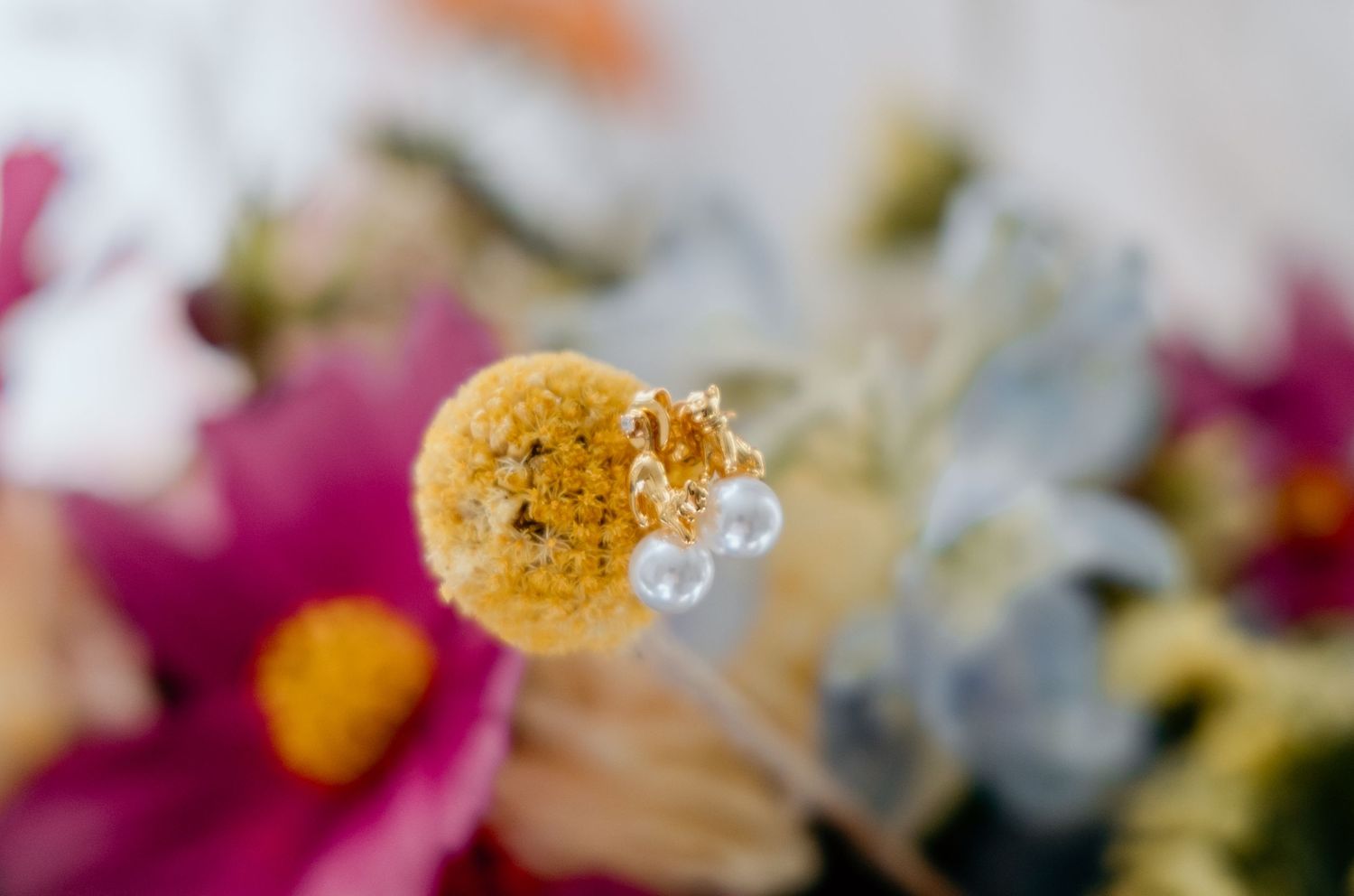 Close-up of a yellow billy ball flower with pearl earrings, surrounded by colorful blooms in soft focus.