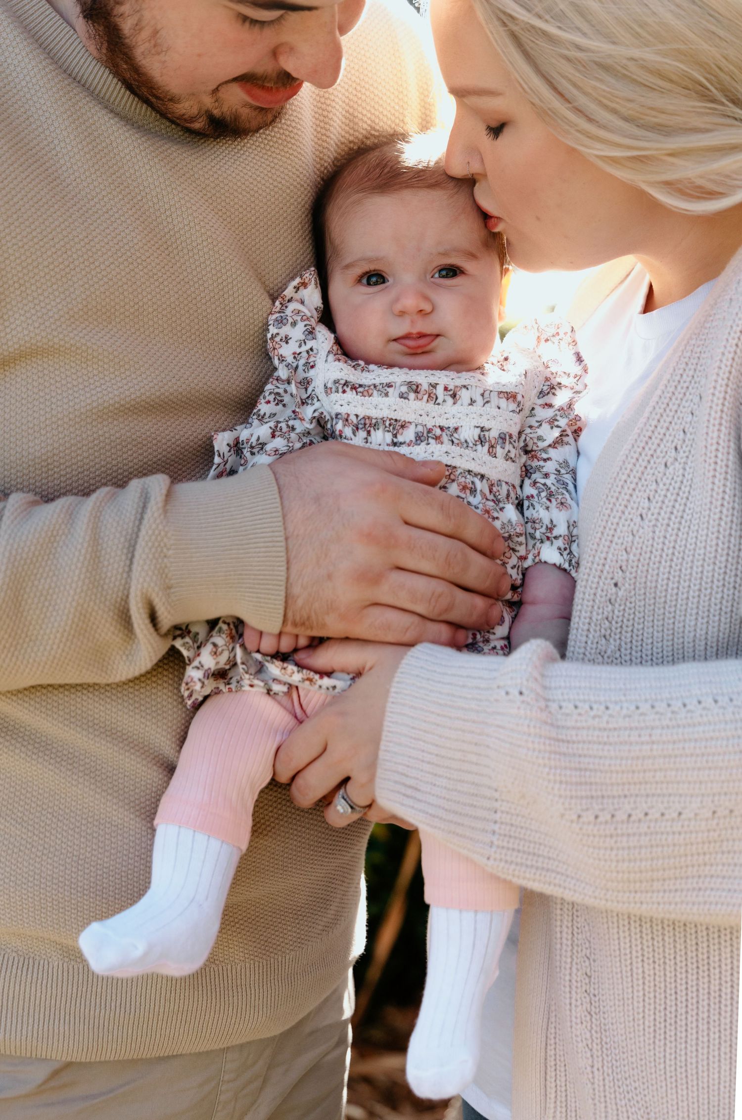 A series of tender moments showing a baby in a floral dress being held in someone's arms wearing a white sweater.