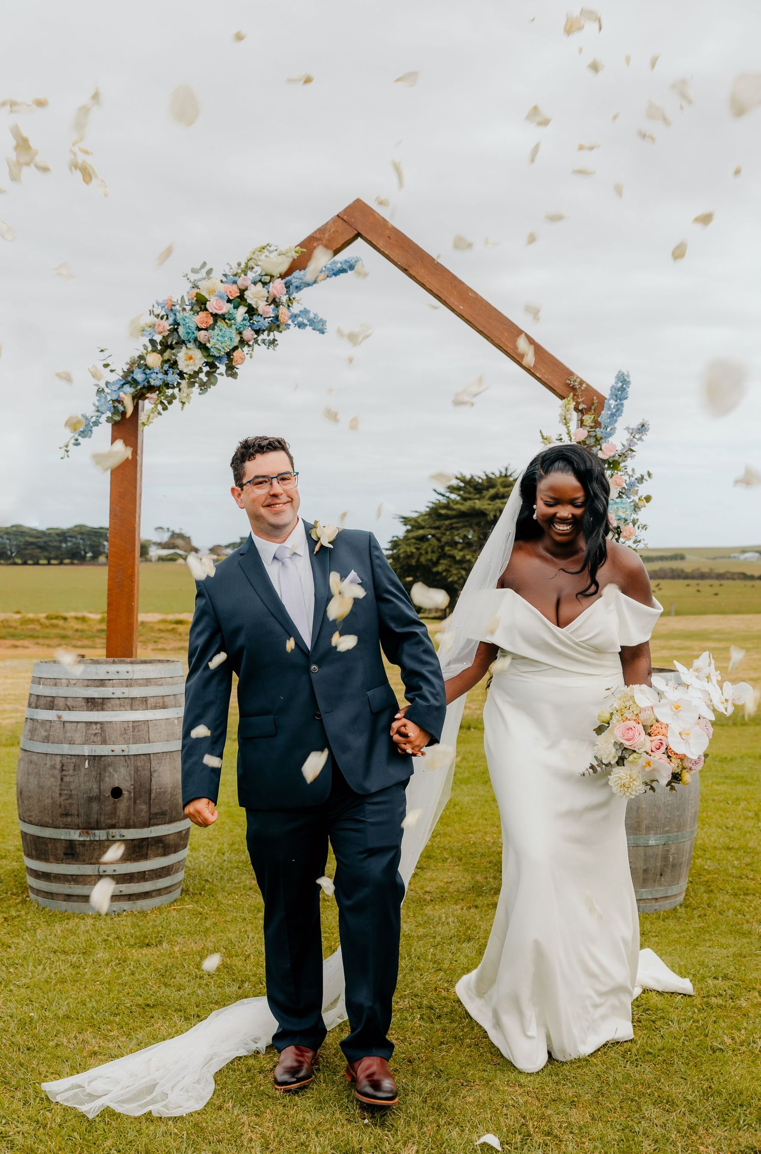 A joyful couple celebrates under a wooden arch at their outdoor wedding ceremony with wine barrels and floral decor.