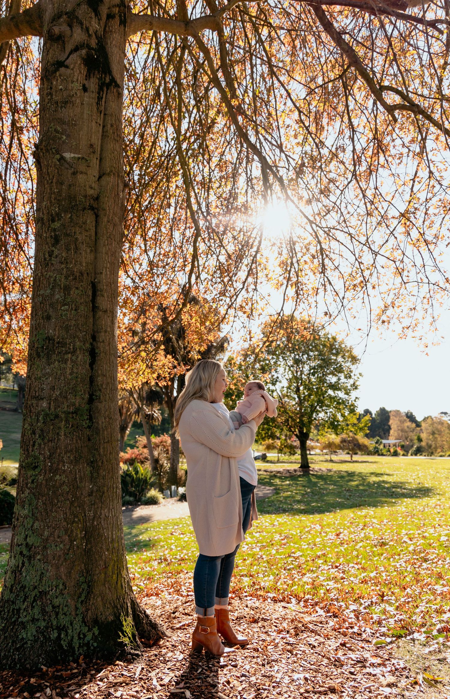 A couple embraces under autumn trees with golden leaves falling in a sunlit park setting.