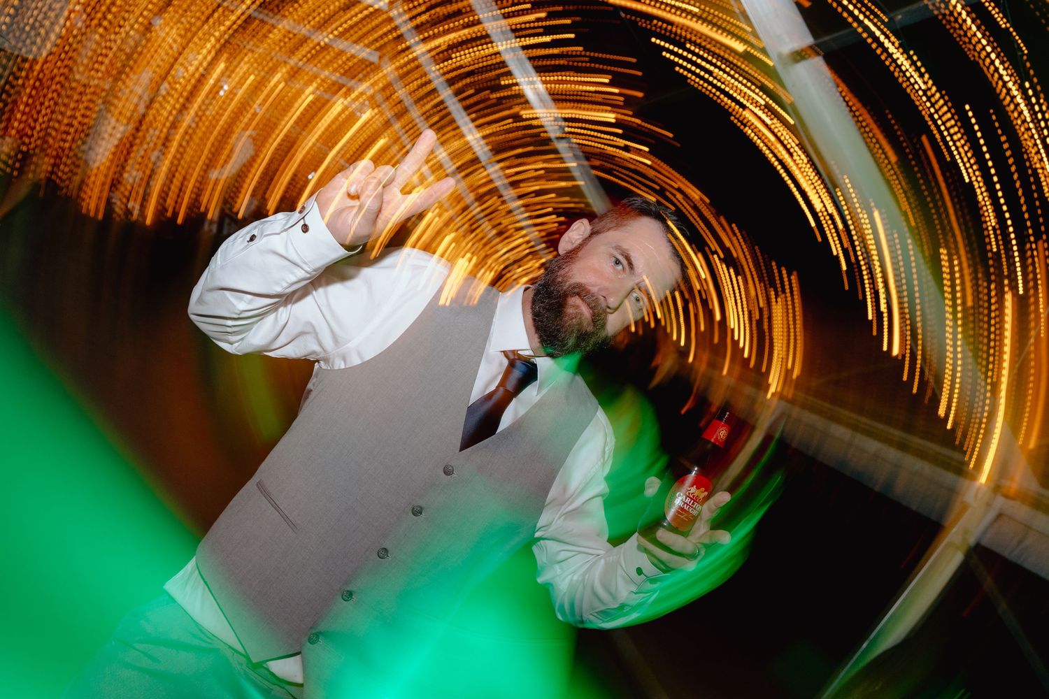 Long exposure photograph showing circular light trails in orange and green against a dark background.