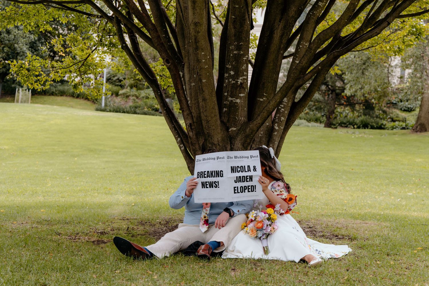 Someone sleeping under a blanket on green grass in a peaceful park setting during daytime.