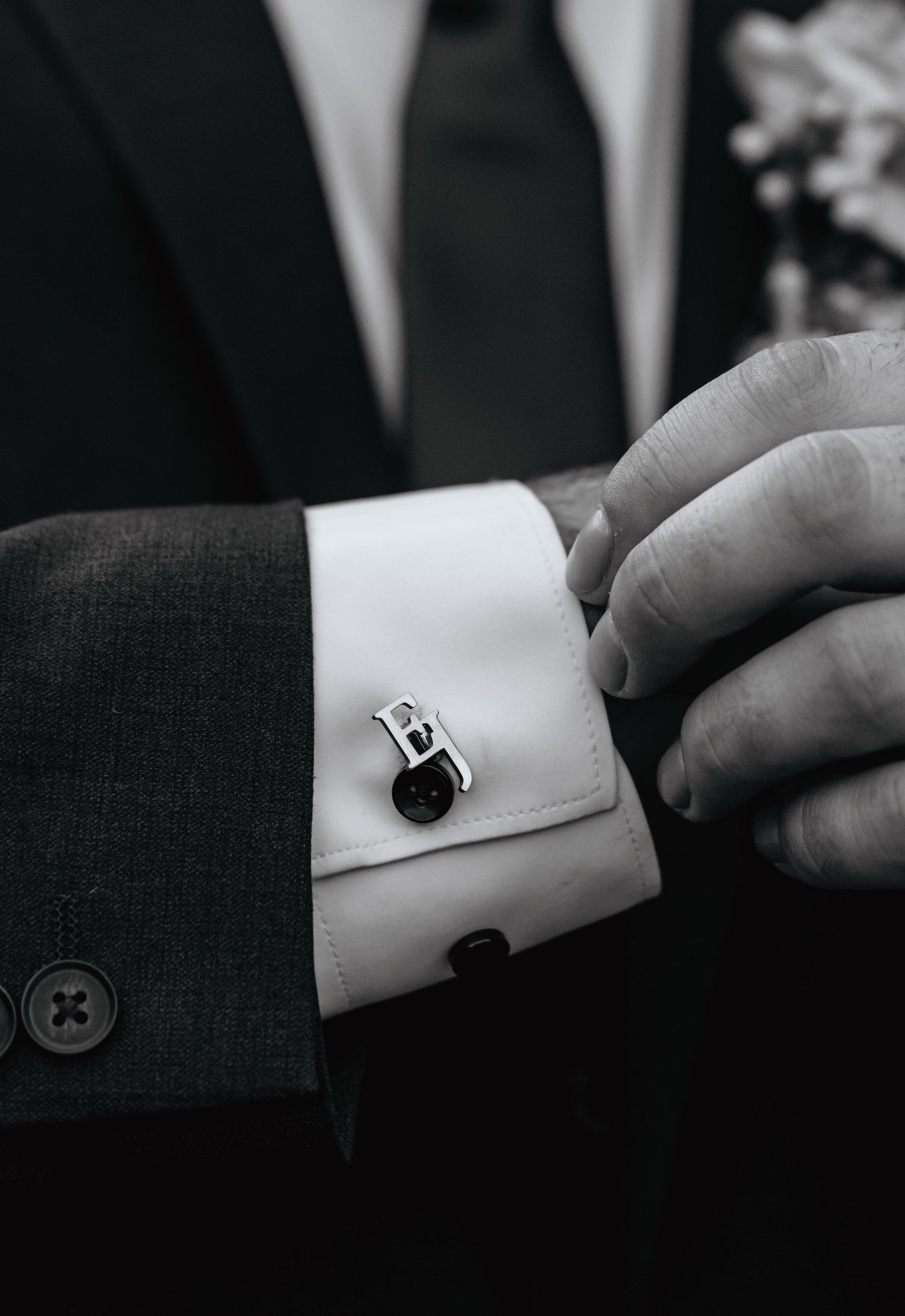 Black and white photo of a groom adjusting his monogrammed silver cufflinks on a white dress shirt.