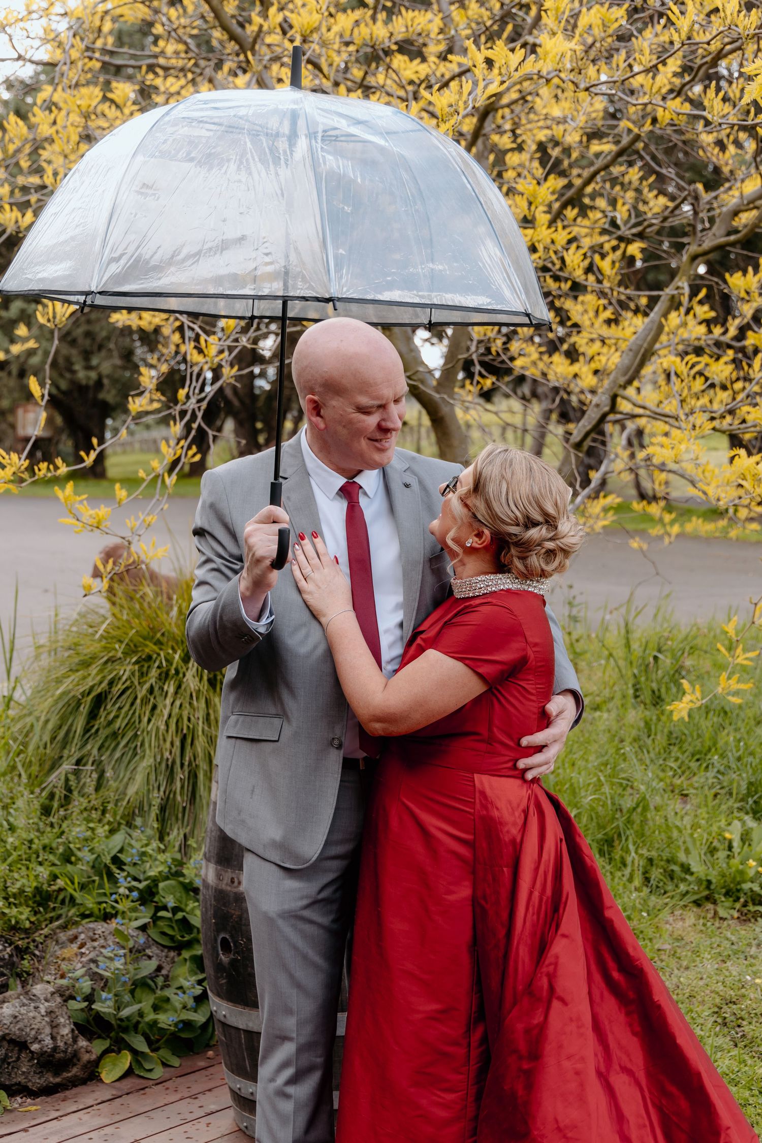 A couple shares a romantic moment under a clear umbrella against a backdrop of yellow autumn foliage.