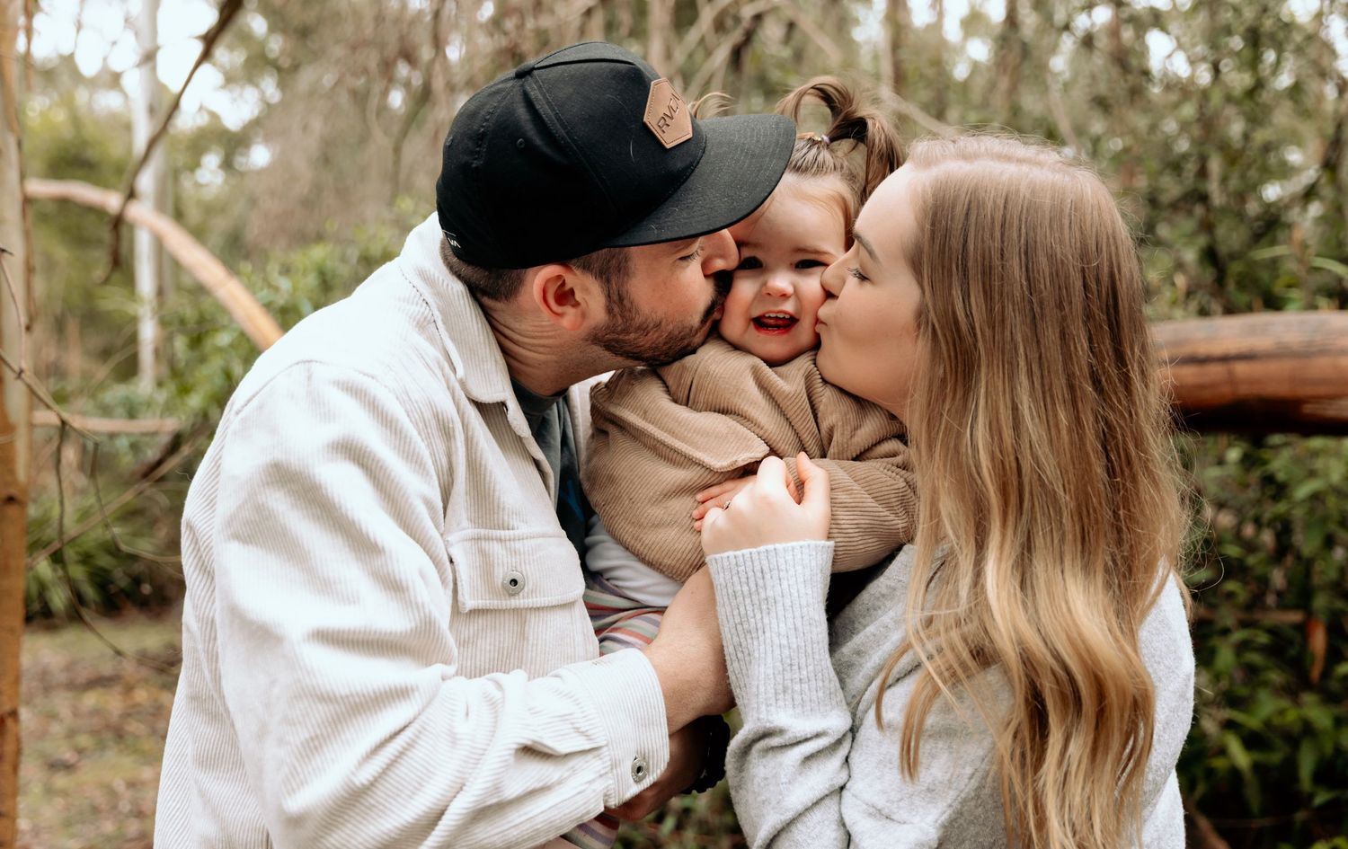 A heartwarming family moment captured outdoors with a toddler being embraced by parents.
