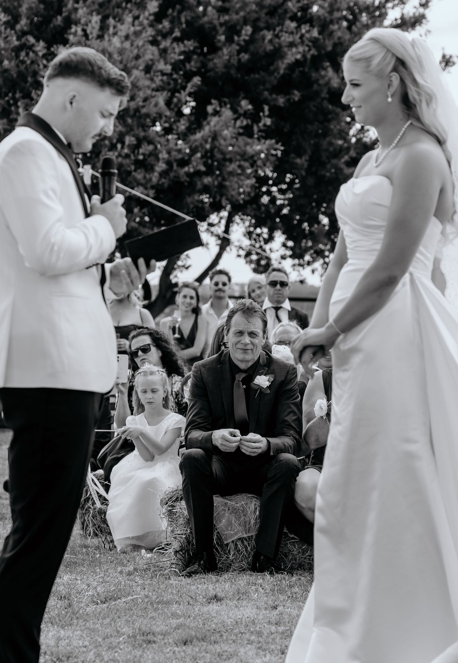 Black and white outdoor wedding ceremony with bride and groom exchanging vows before seated guests.