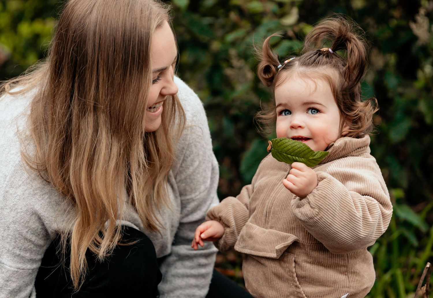 Parent and toddler share loving moment outdoors among greenery.