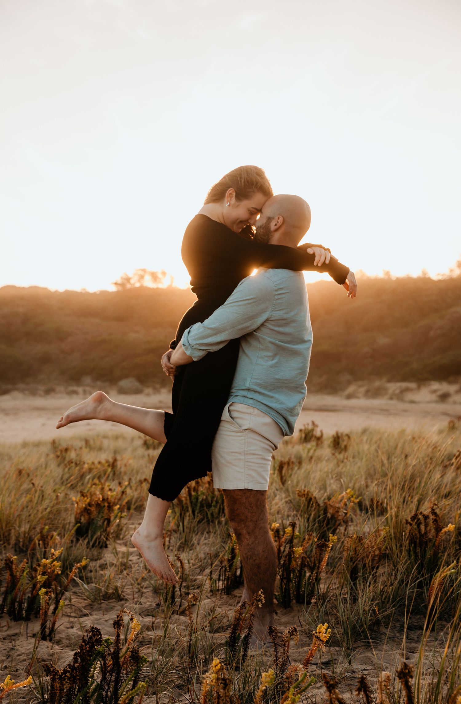 Couple embracing in golden sunset light among wildflowers.