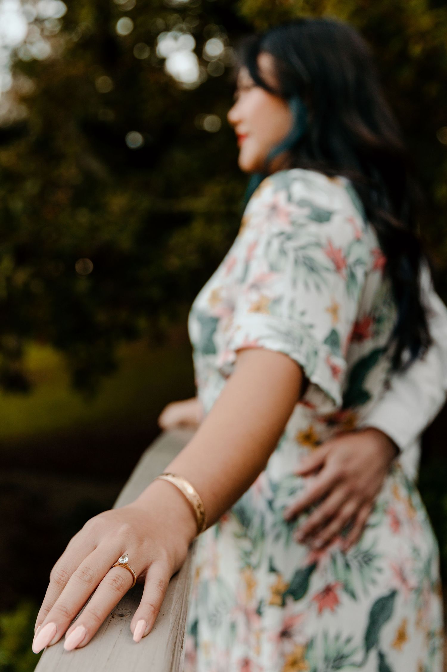 Close-up of a floral dress and engagement ring in a dreamy outdoor setting.