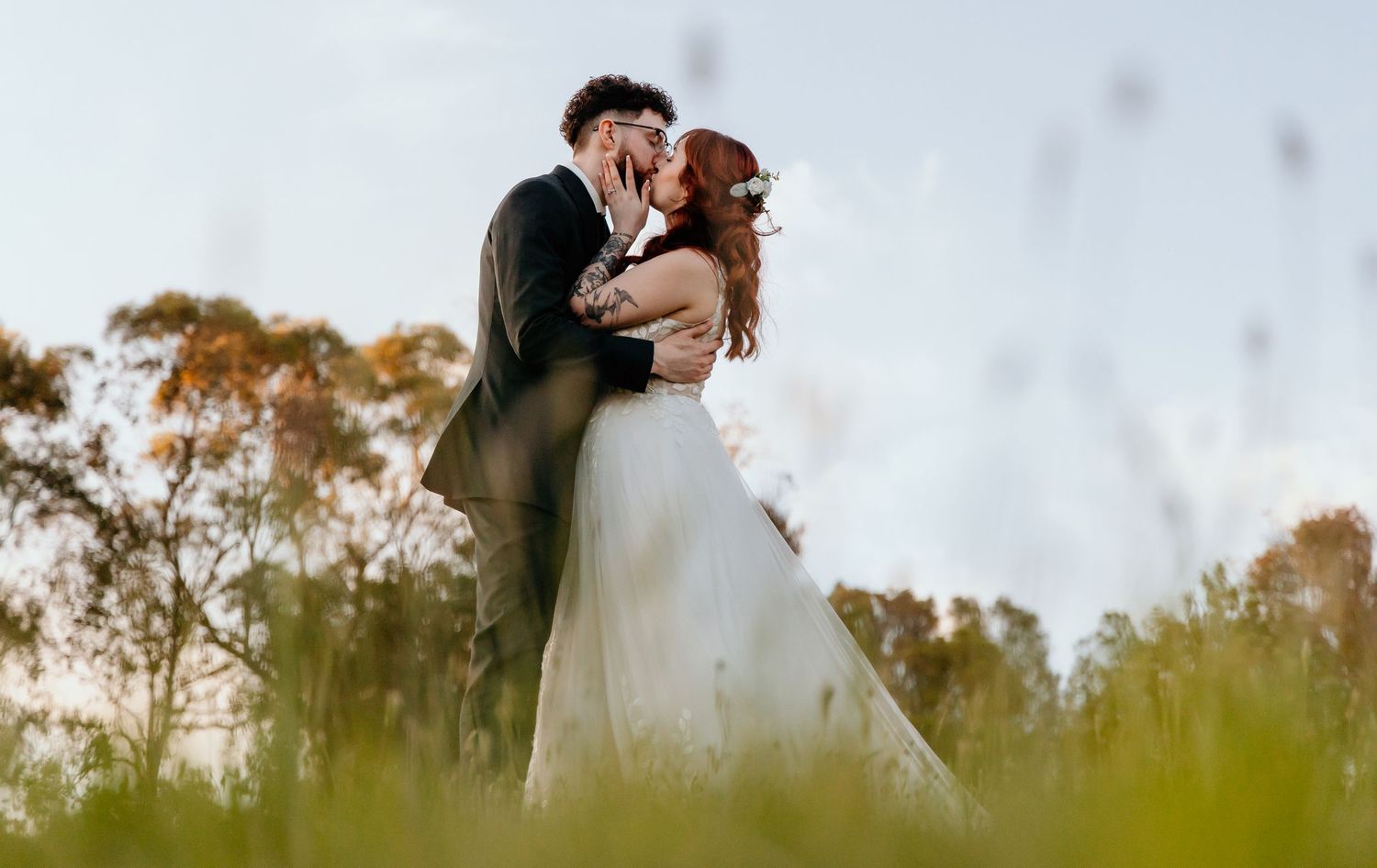 A romantic outdoor wedding moment captured at a scenic location during a dreamy golden hour with trees in the background.