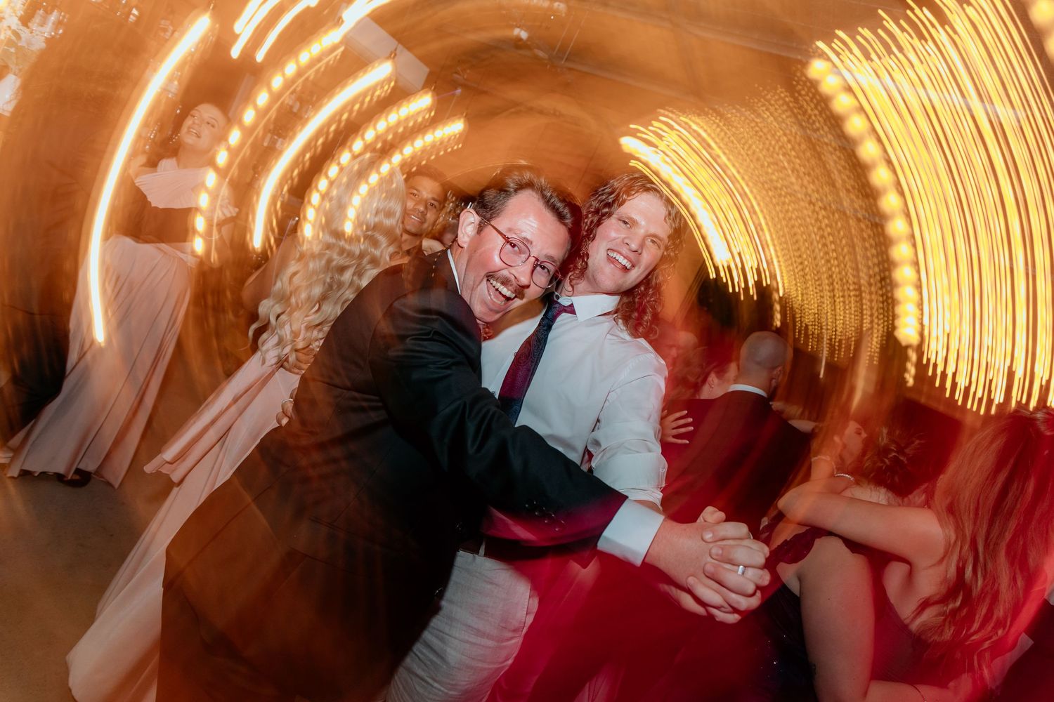 Dancing couple in motion at a party venue with glowing golden light trails creating a dynamic tunnel effect.