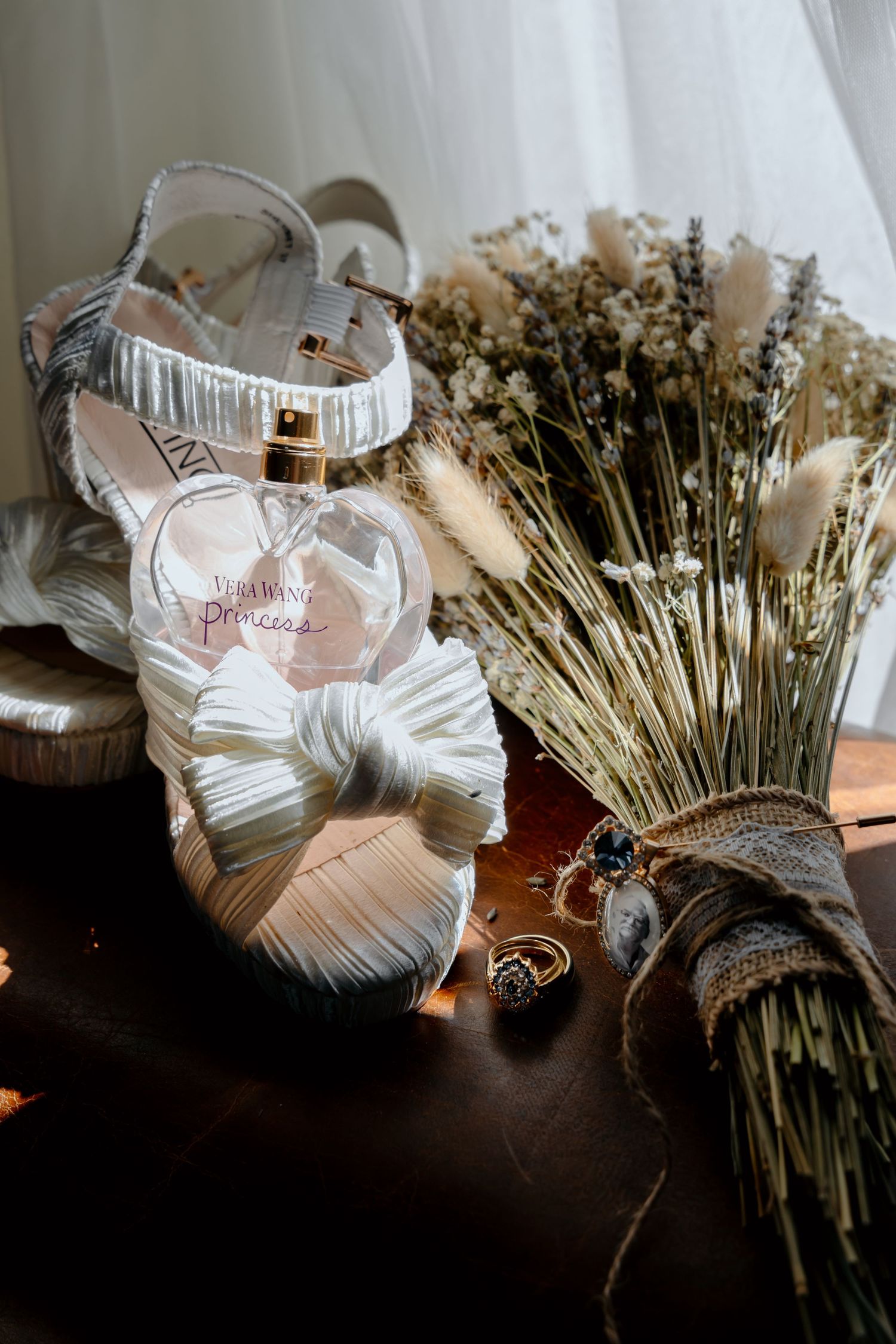 Elegant white bridal shoes displayed next to a rustic dried flower bouquet on a dark wooden surface.