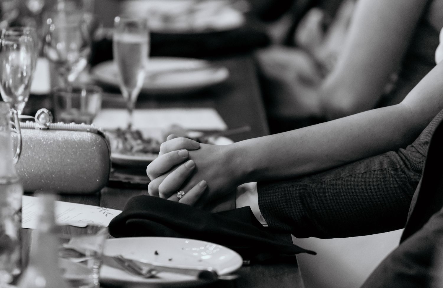 Black and white photo of couple holding hands at elegant dinner table with glassware.
