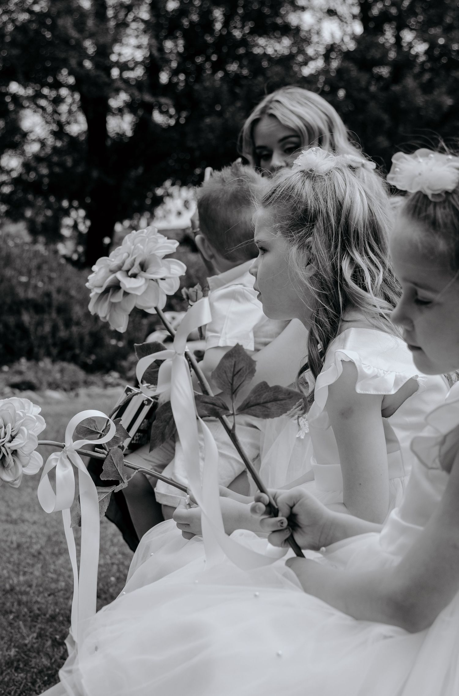 Black and white photo of flower girls in white dresses holding floral wands at a wedding ceremony.