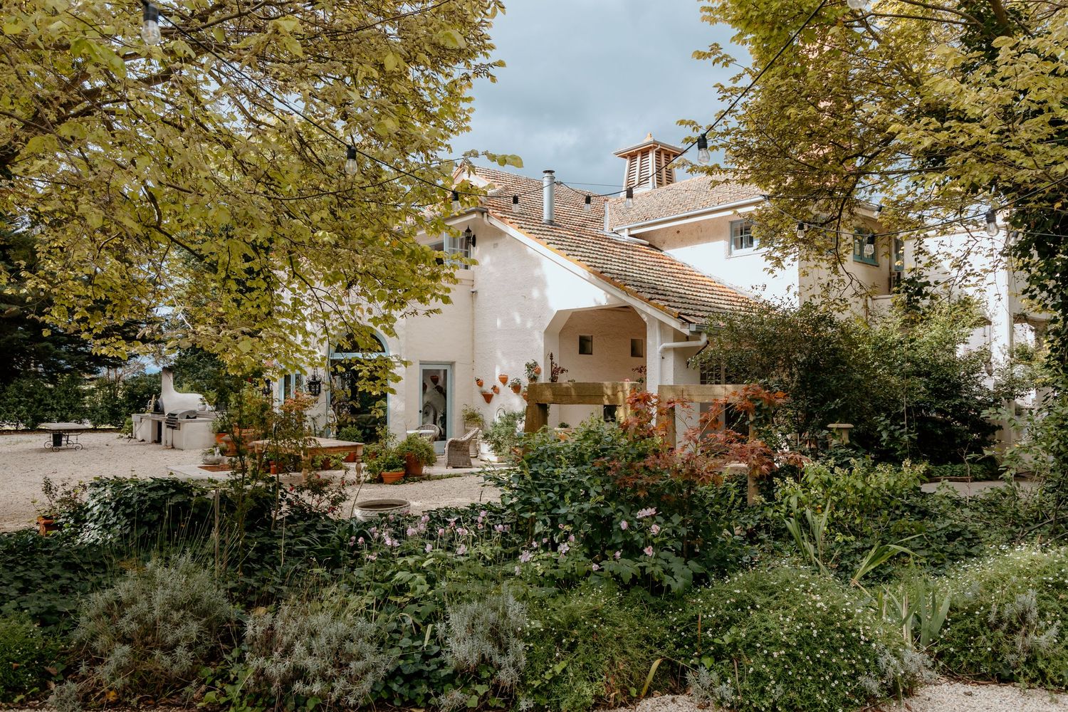 Charming white Mediterranean villa surrounded by lush green gardens and mature trees.