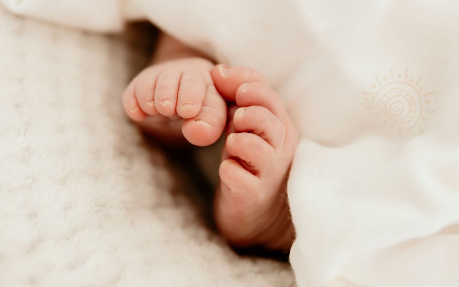 Close-up photo of delicate newborn baby toes against soft white fabric.