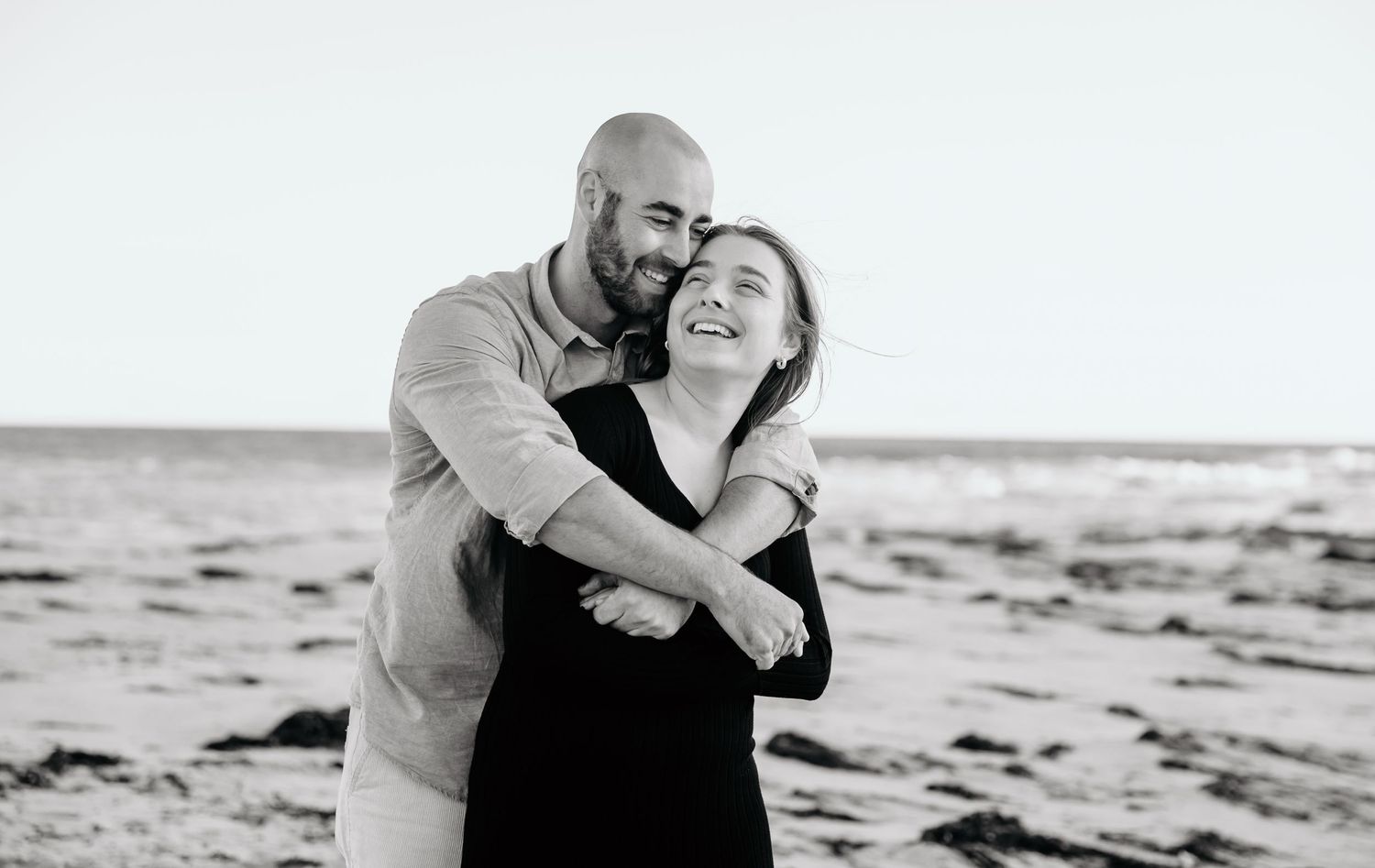 Intimate black and white portrait of couple embracing on beach.
