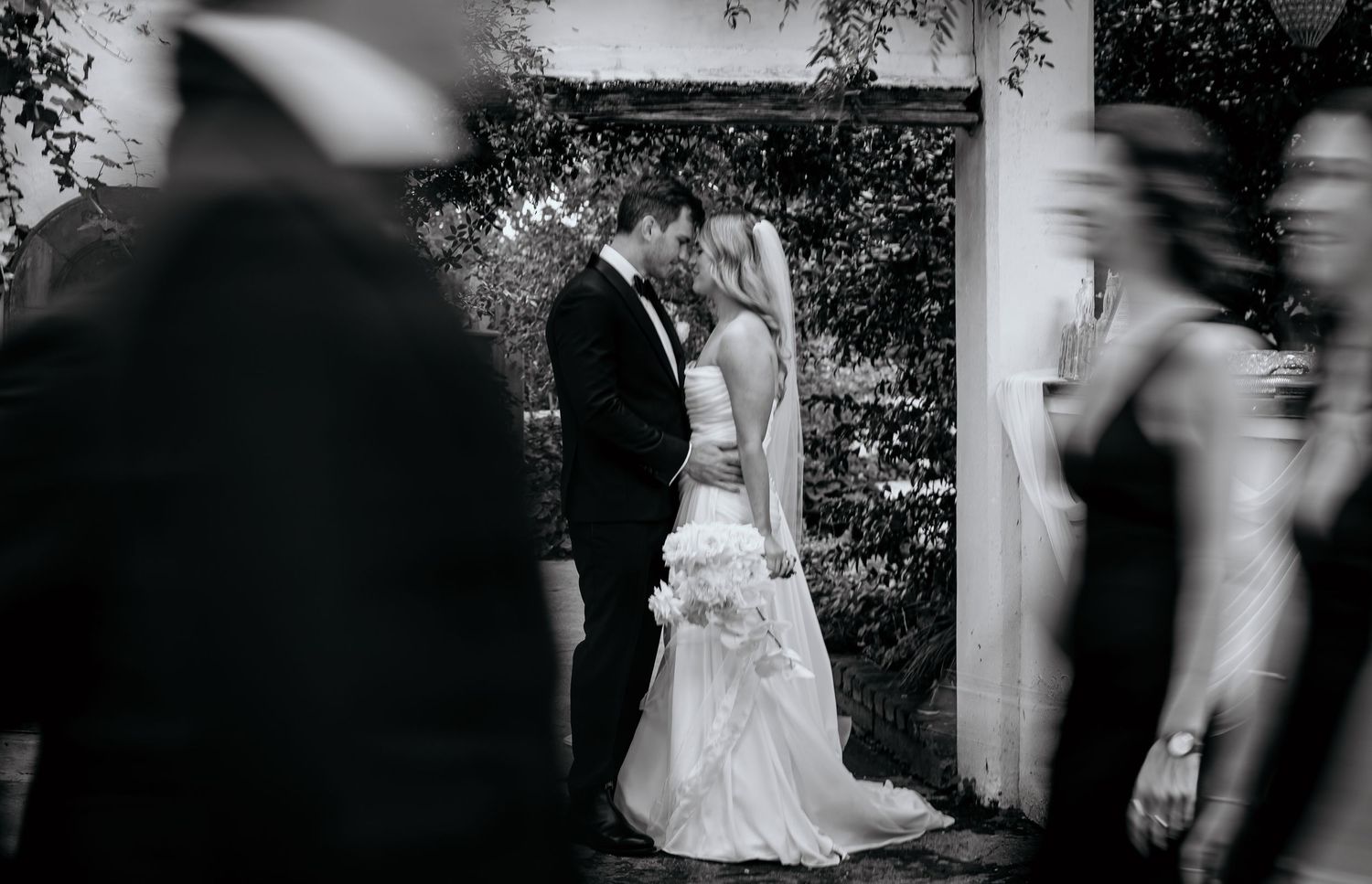 Black and white photo of bride and groom sharing a kiss at outdoor wedding ceremony.